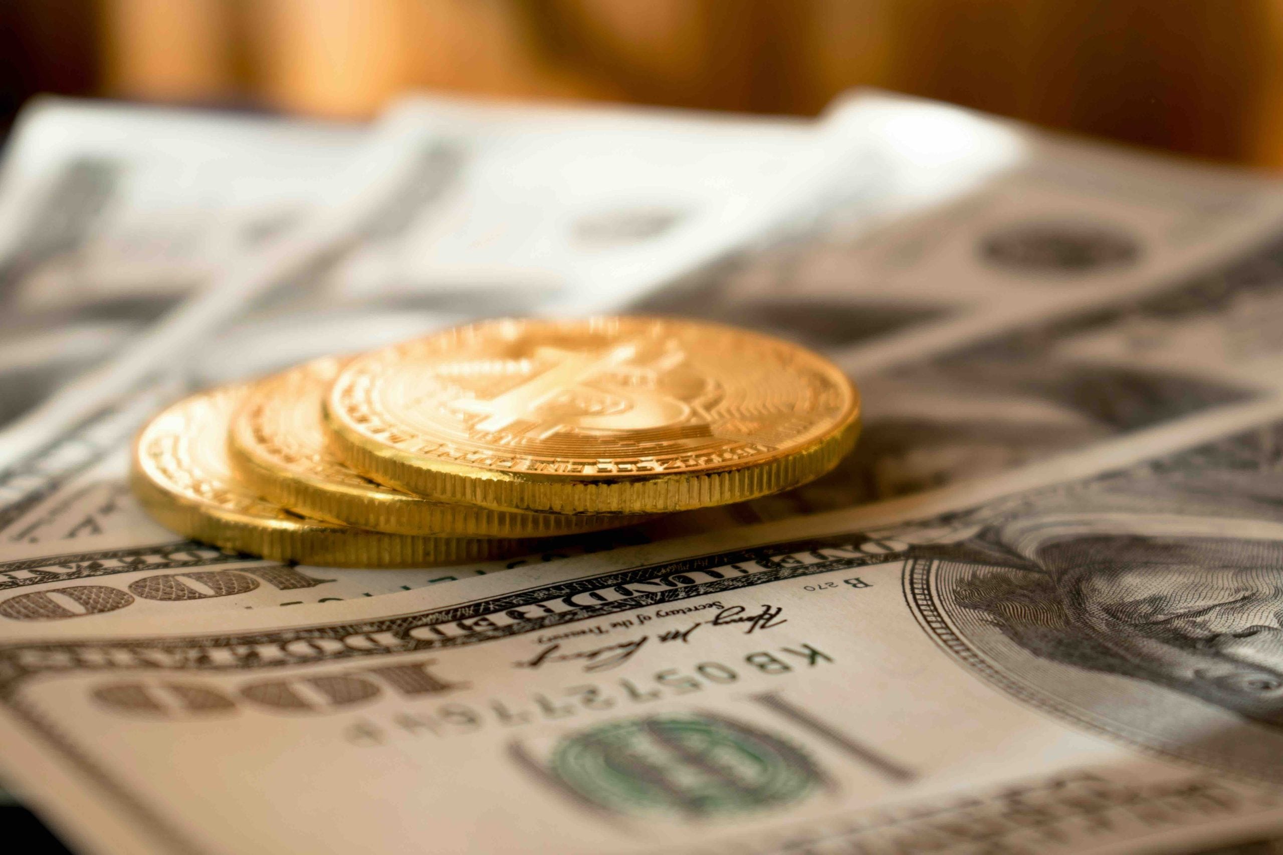 Three gold-colored coins stacked on top of several US one-hundred-dollar bills.