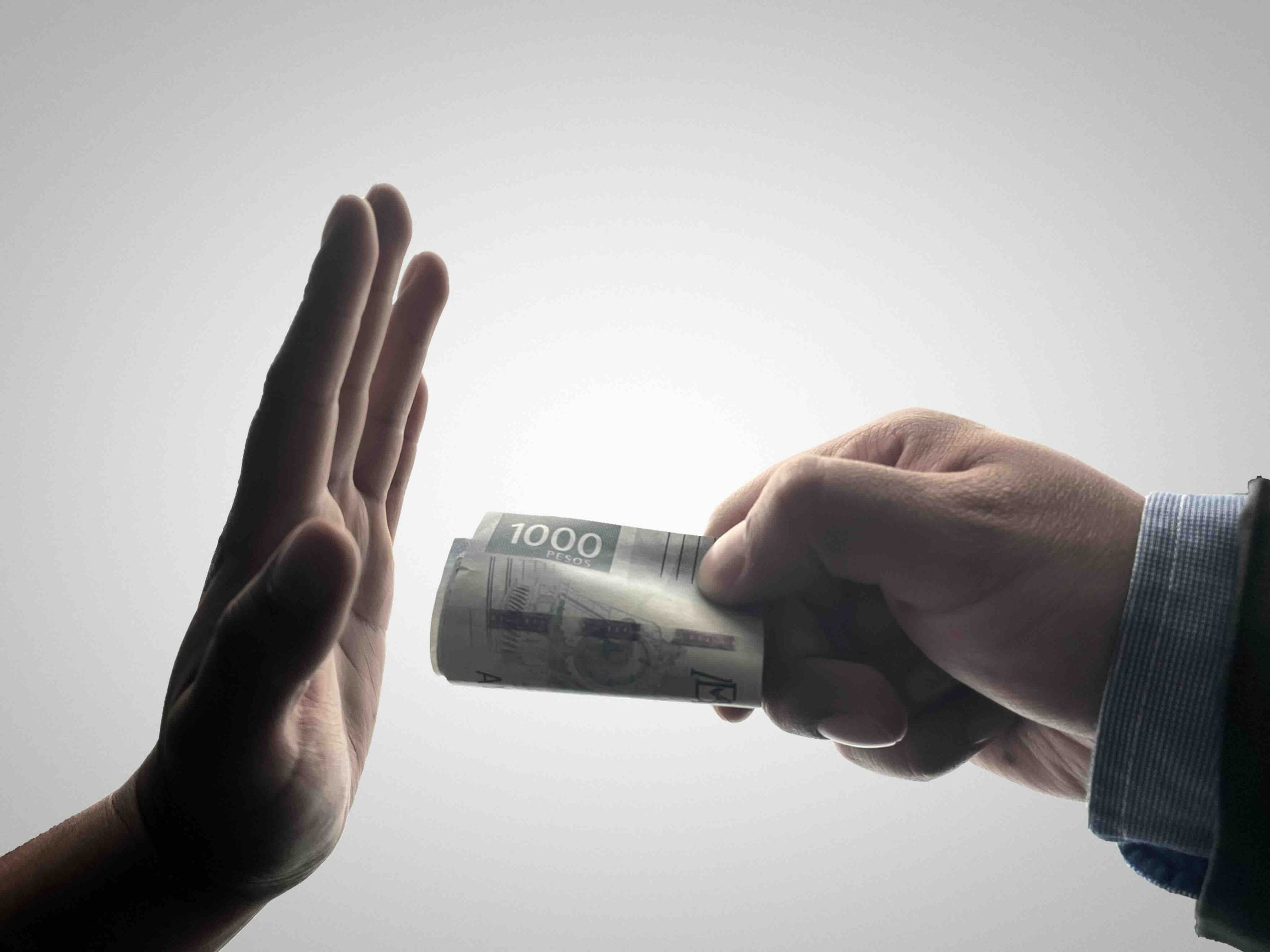 A person’s hand held up in a gesture of refusal toward another hand offering a 1,000-peso banknote.