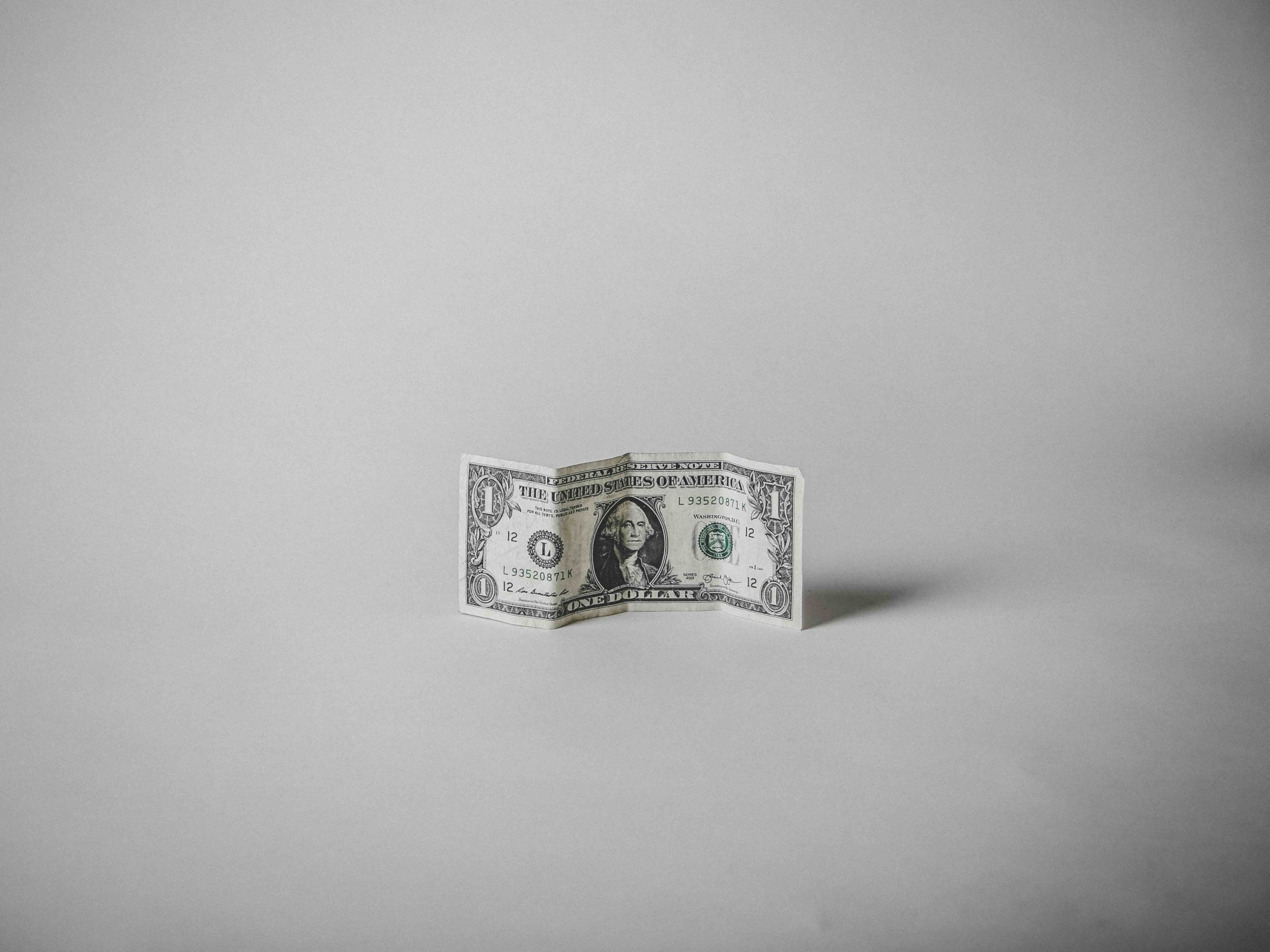 A single United States one-dollar bill folded to stand upright on a plain background.