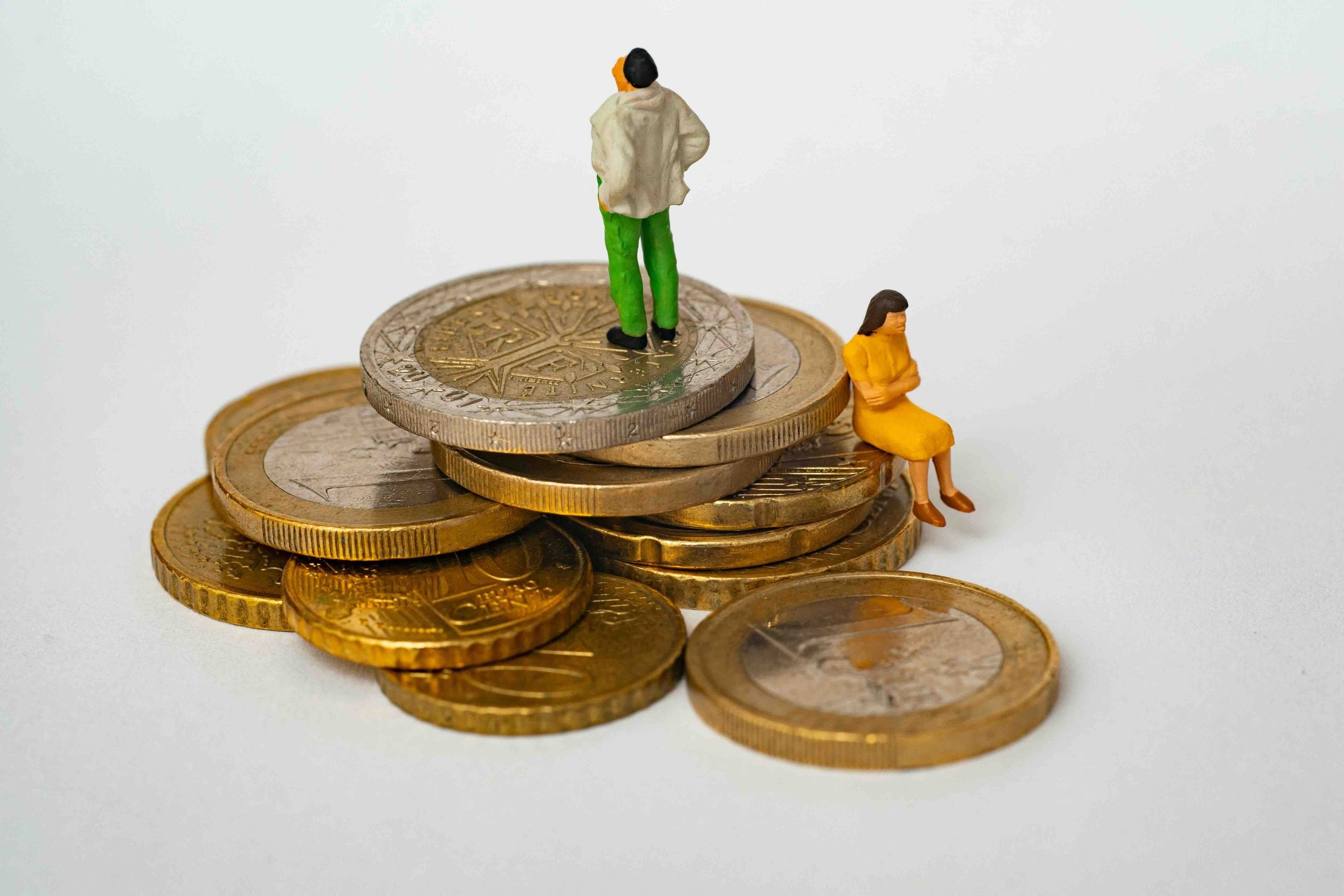 Two miniature figures stand and sit on a small pile of Euro coins.