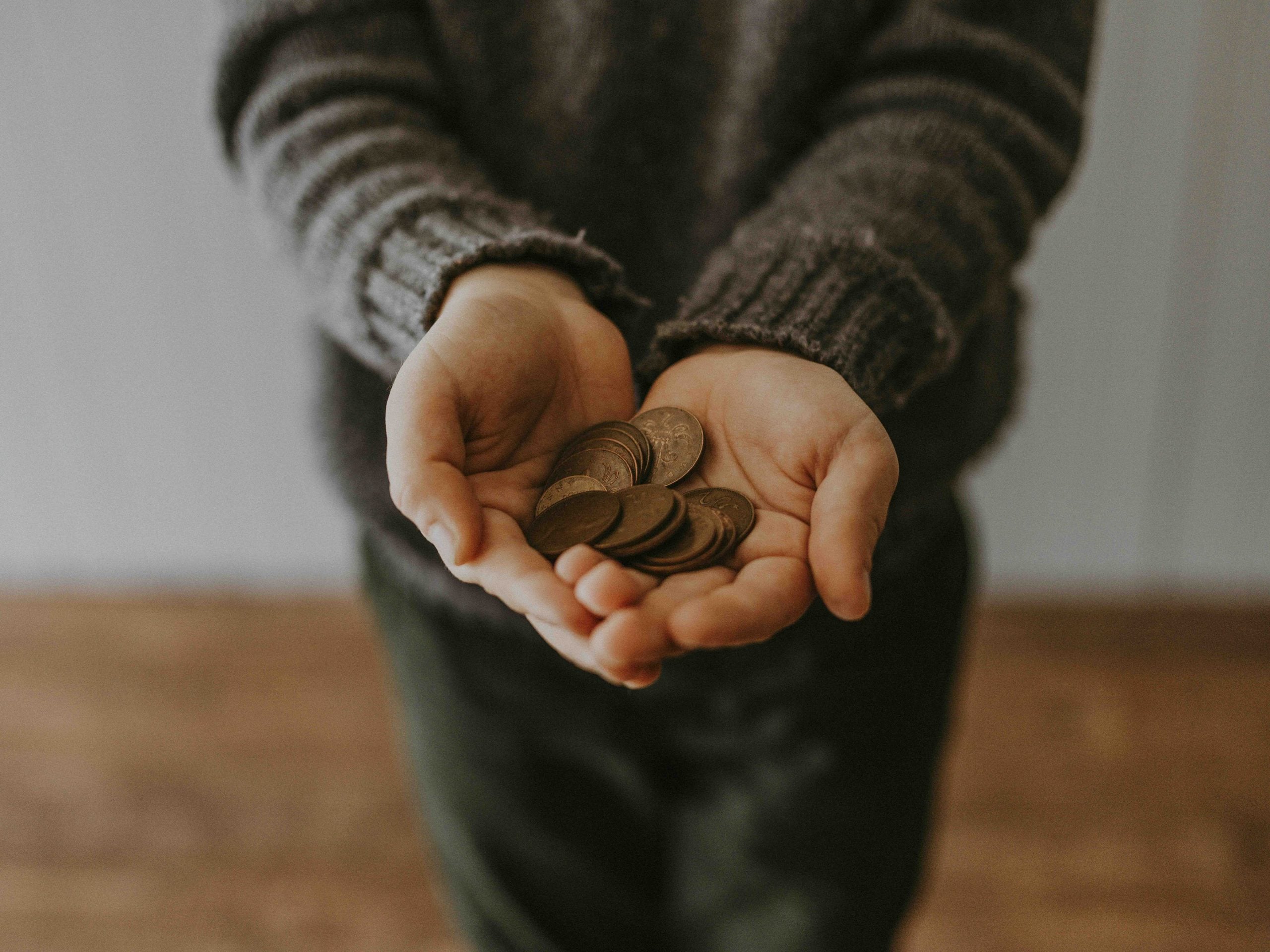 Person wearing a sweater holding a handful of coins in their cupped palms.