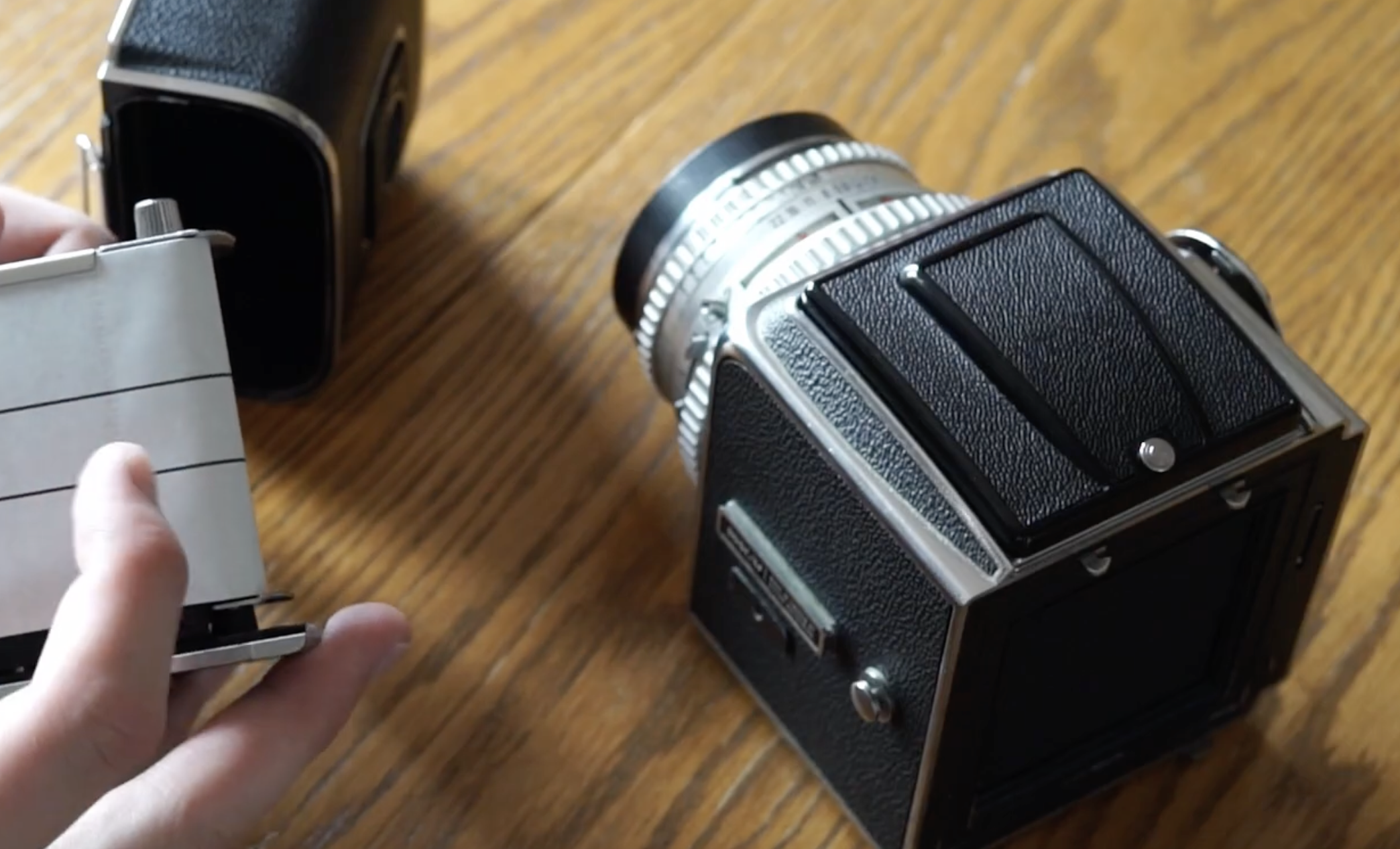 A person holding the film insert for a medium-format camera sitting on a wooden table.