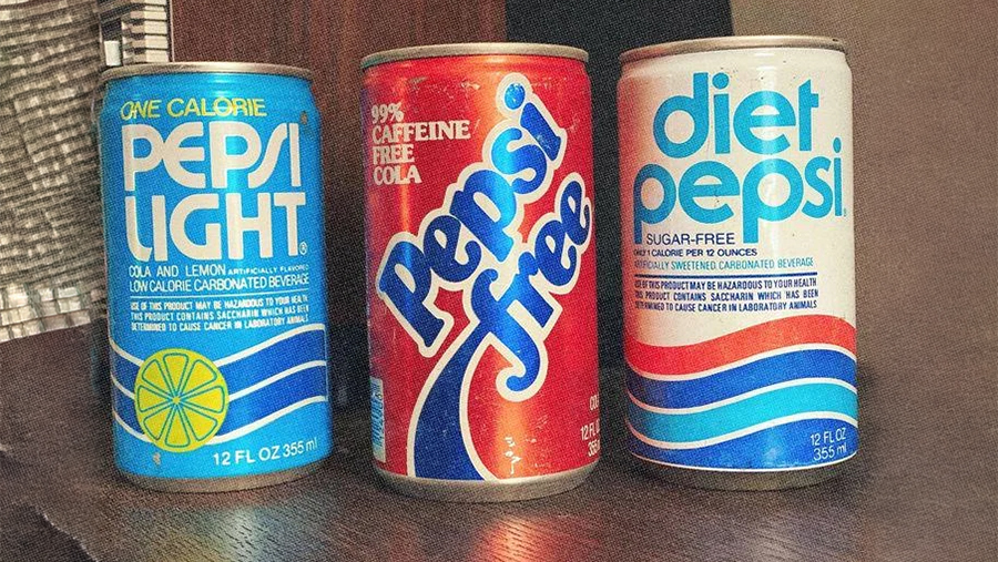 Three vintage soda cans: Pepsi Light (blue, with lemon), Pepsi Free (red, caffeine free), and Diet Pepsi (blue and white), displayed on a wooden surface.
