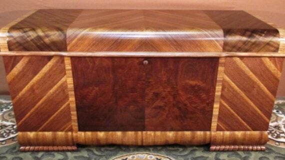 A rectangular wooden chest featuring contrasting wood veneers in geometric patterns and a central keyhole.