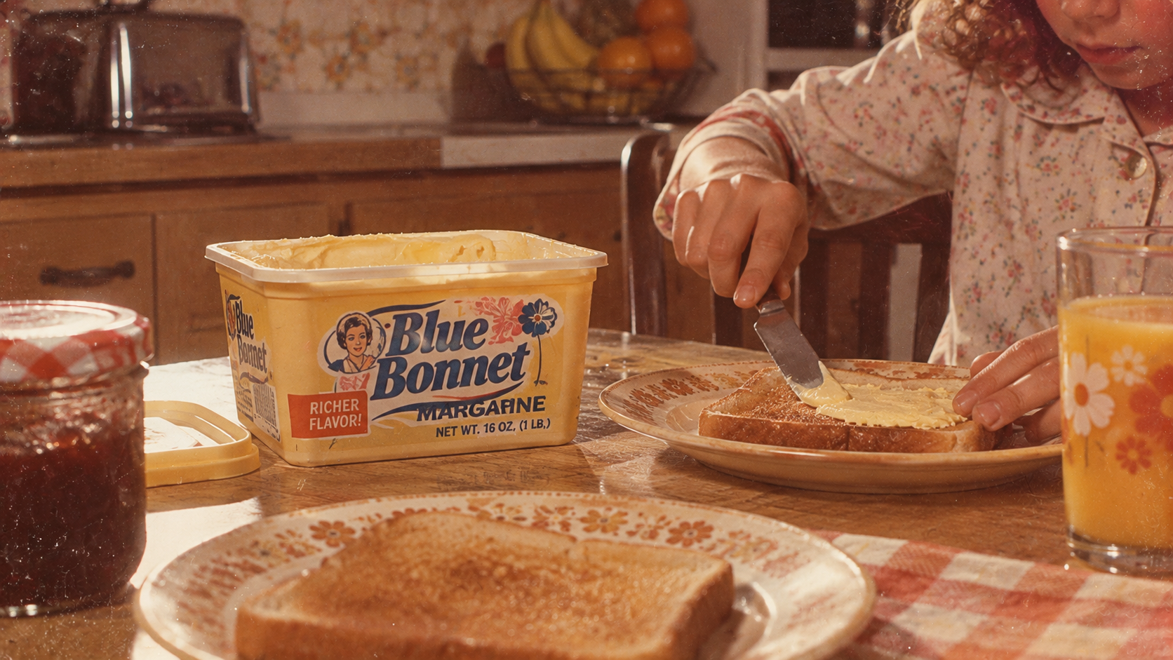A person spreads Blue Bonnet margarine onto a slice of toast at a kitchen table.