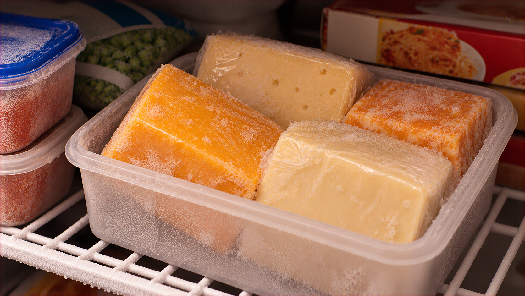 A plastic container holding several wrapped blocks of frozen cheese inside a freezer.