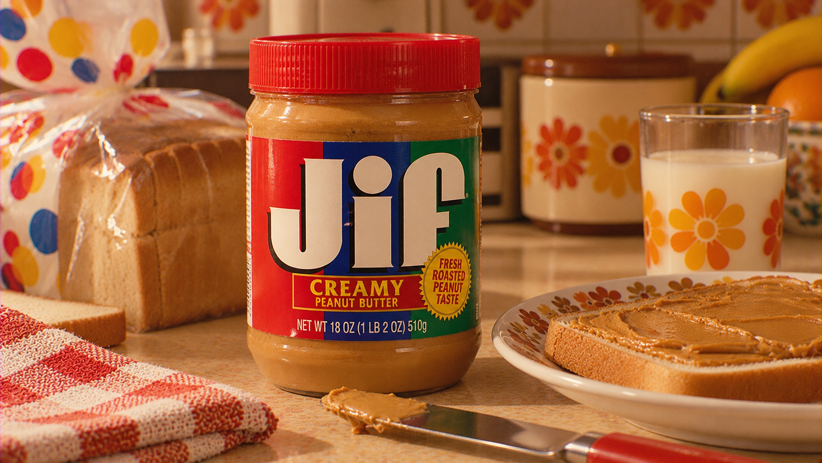 A jar of Jif creamy peanut butter is on a kitchen counter next to sliced bread, a glass of milk, a plate with a peanut butter sandwich, and a knife with peanut butter.