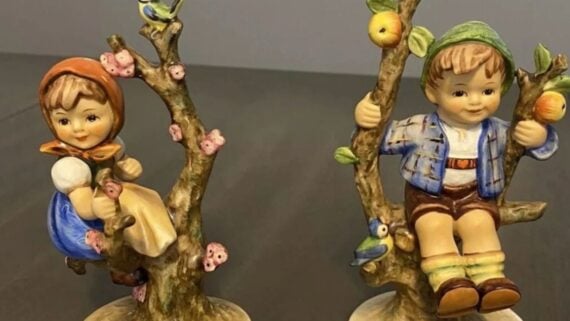 Two Hummel figurines of a girl and a boy perched in apple trees.