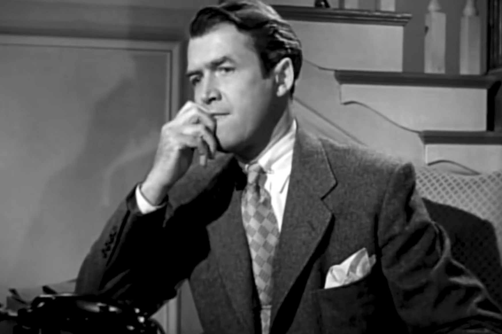 A man in a suit and tie sits with his hand near his chin, appearing to be in deep thought.