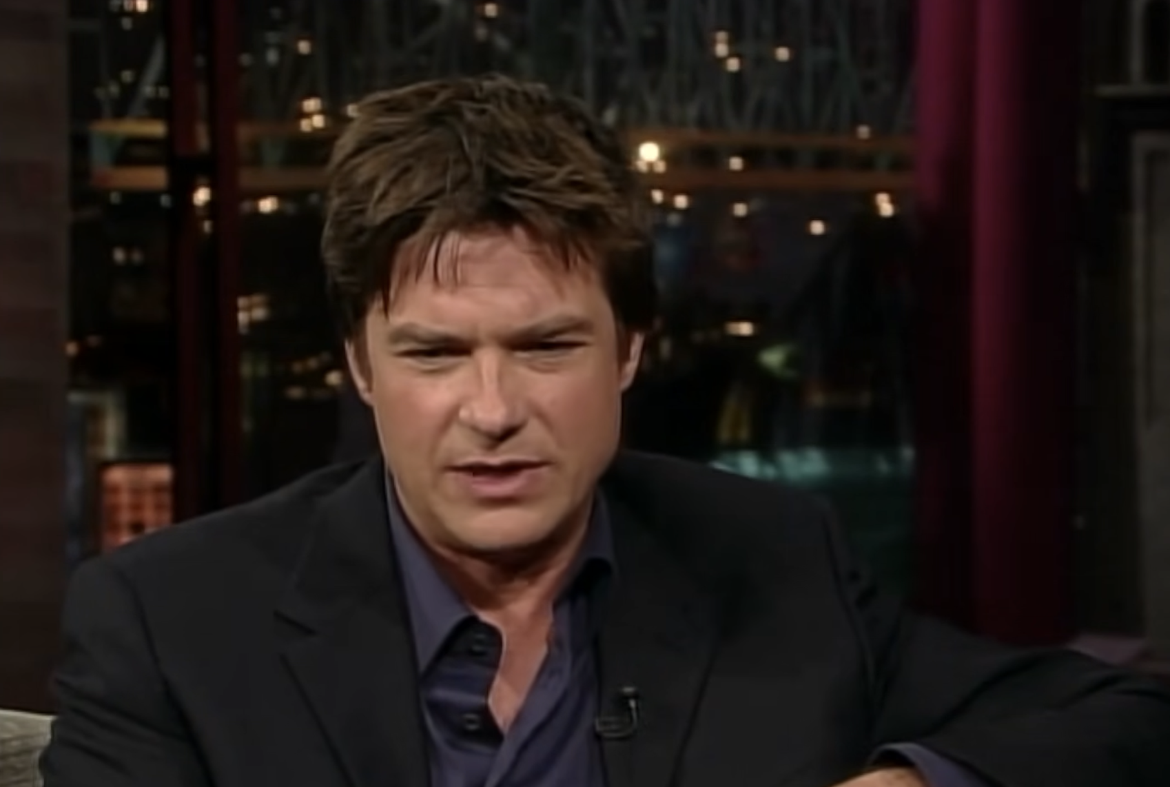 Jason Bateman sits in a chair during a television interview.