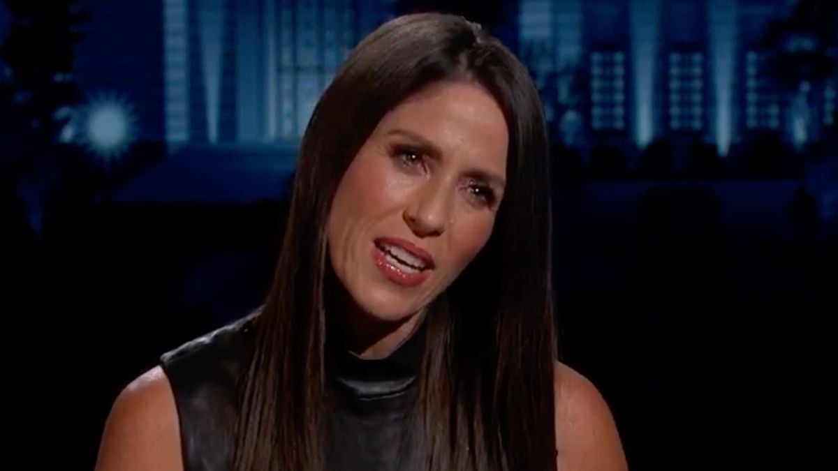 A woman with long dark hair speaking against a dark, out-of-focus background.