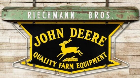 Vintage metal sign reading “Riechmann Bros.” above a larger John Deere logo featuring a leaping deer and the text “Quality Farm Equipment.”