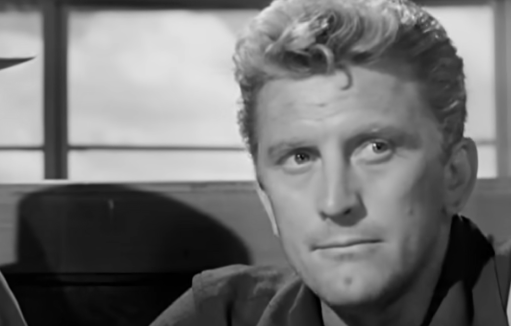 A black and white close-up of actor Kirk Douglas looking forward with a serious expression.