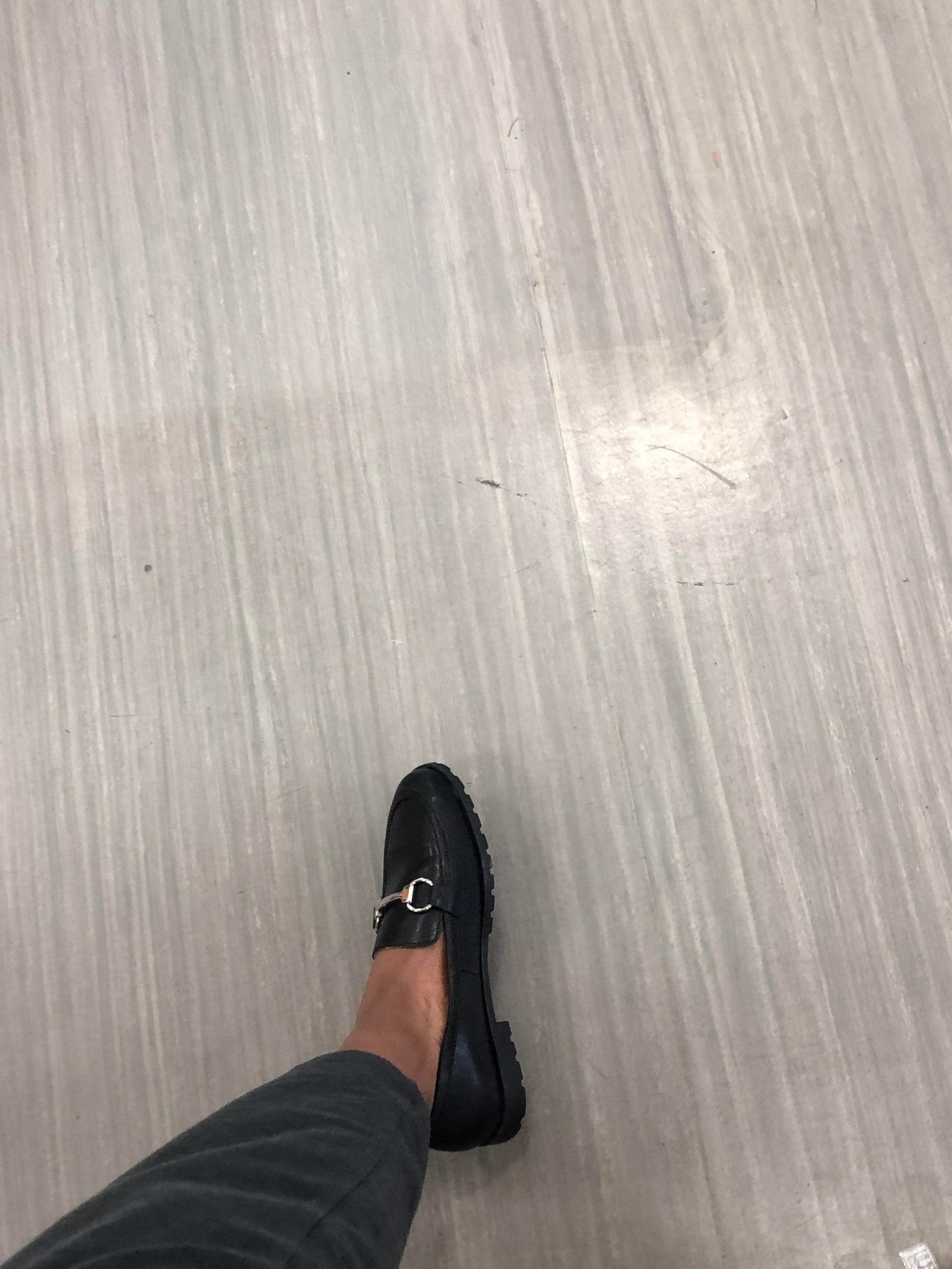 A black loafer with a silver metal bit detail on a light-colored floor.