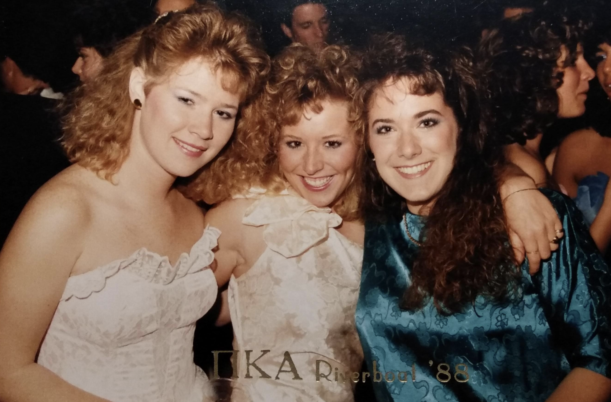 Three young women smiling for a photo at a formal event with “ΠKA Riverboat ’88” printed at the bottom.