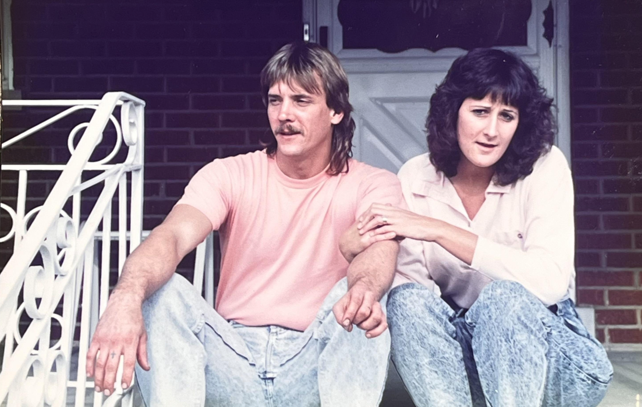 A man with a mustache and a woman sitting together on a porch step.