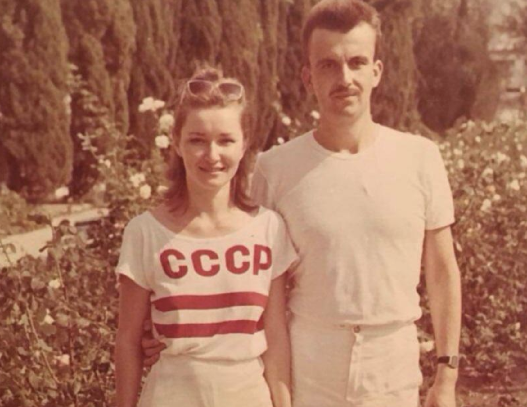 A young man and woman standing together in a park, with the woman wearing a shirt that says “СССР.”