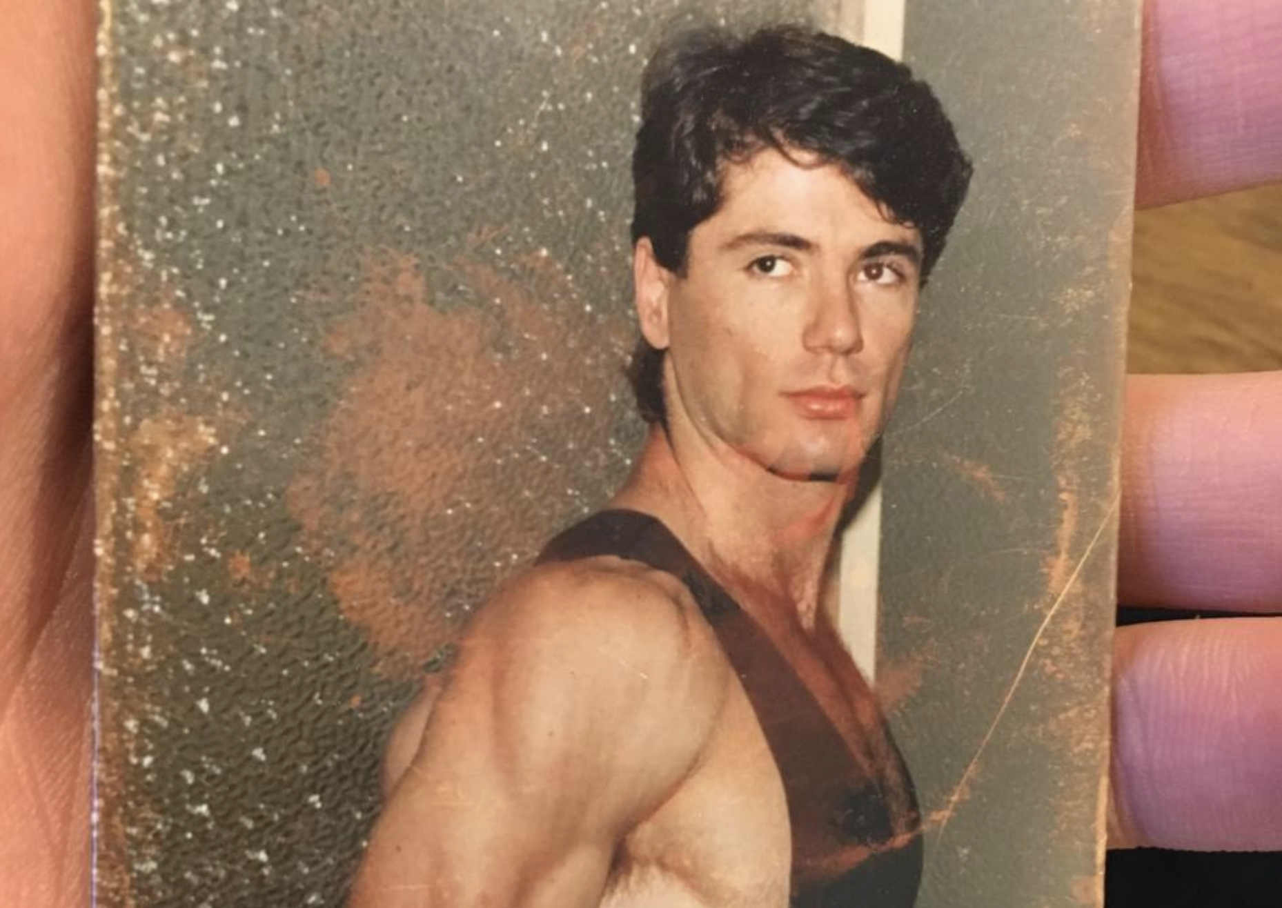 A vintage portrait of a man in a tank top looking over his shoulder.