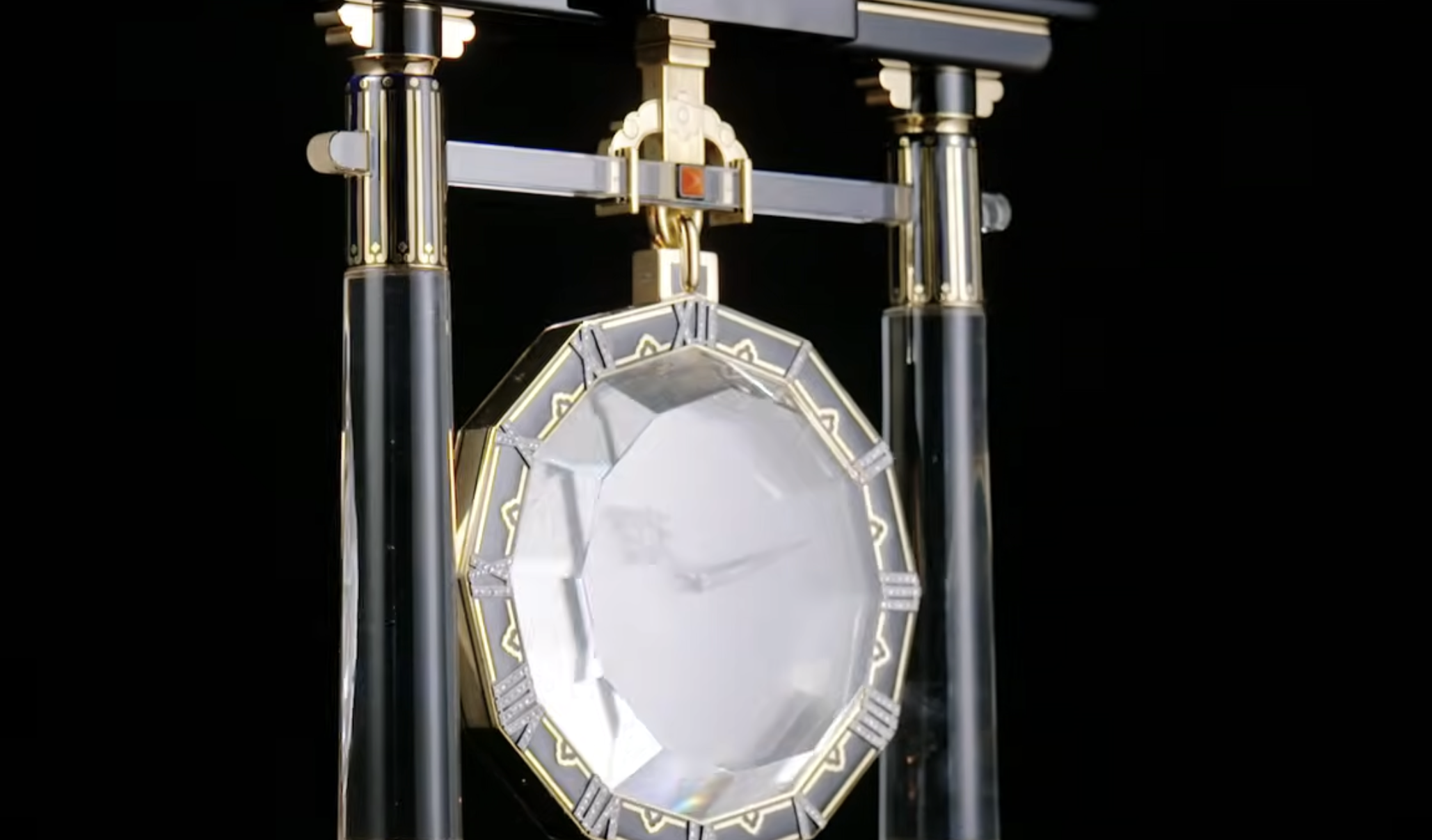 An octagonal, crystal-faced clock suspended within a black and gold frame.