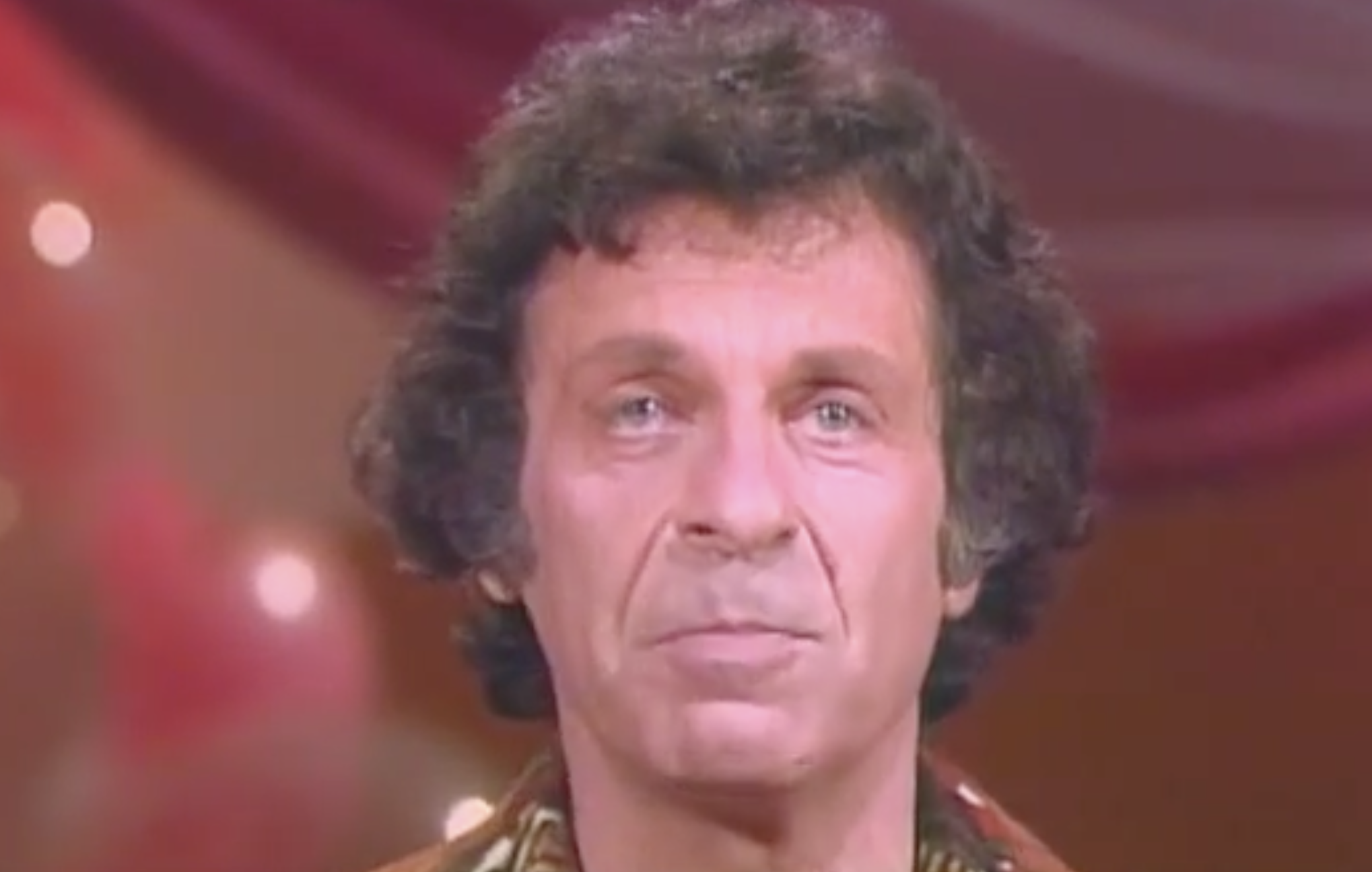 A headshot of a man with dark, wavy hair looking toward the camera.