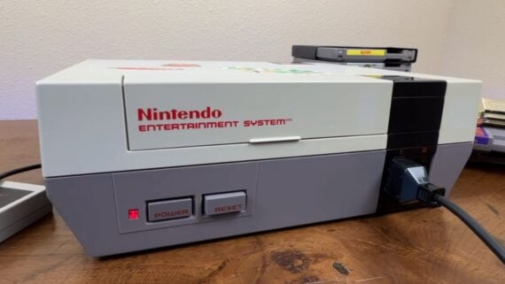 Nintendo Entertainment System console with a game cartridge inserted, sitting on a wooden surface.