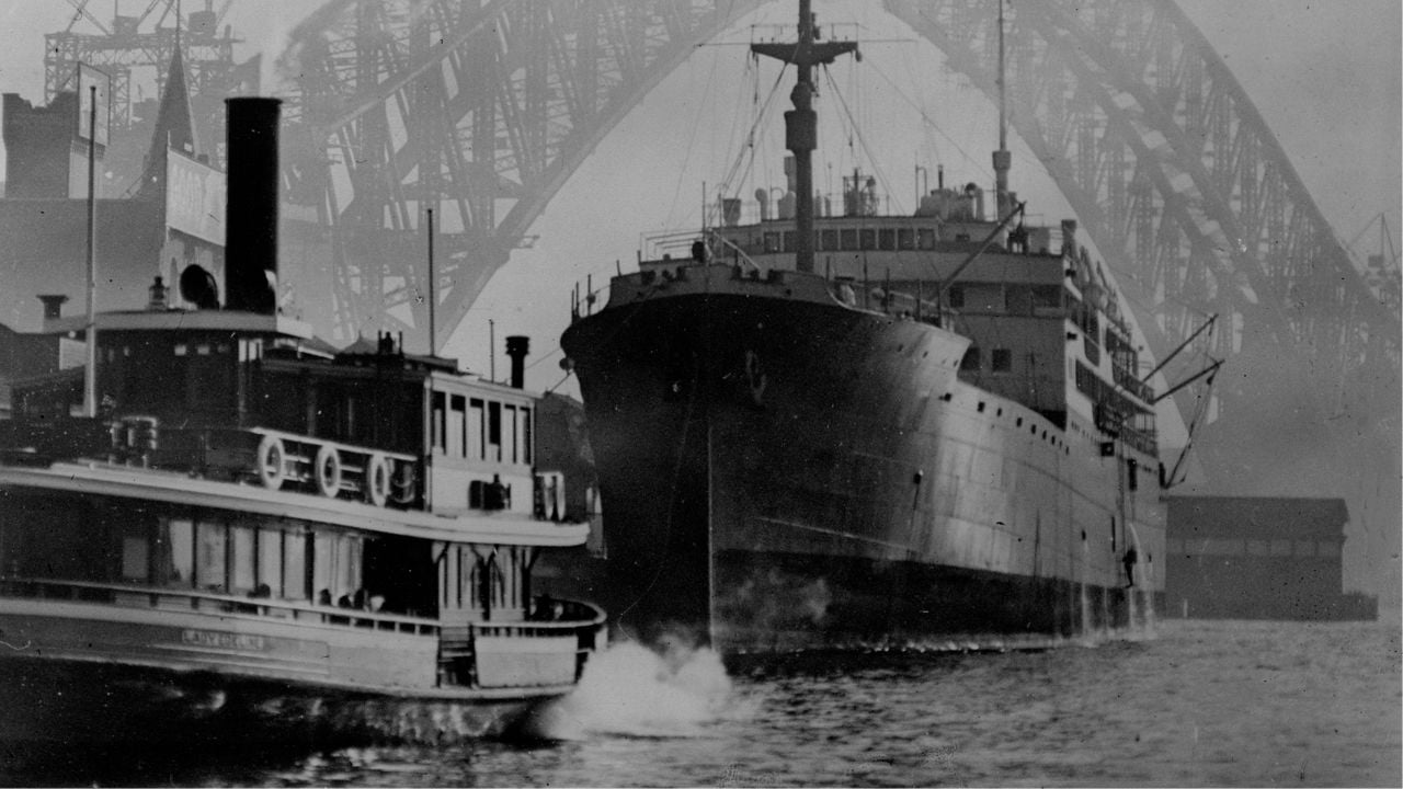 A large ship and a steam ferry travel side by side on the water, with the arch of the Sydney Harbour Bridge visible in the foggy background.