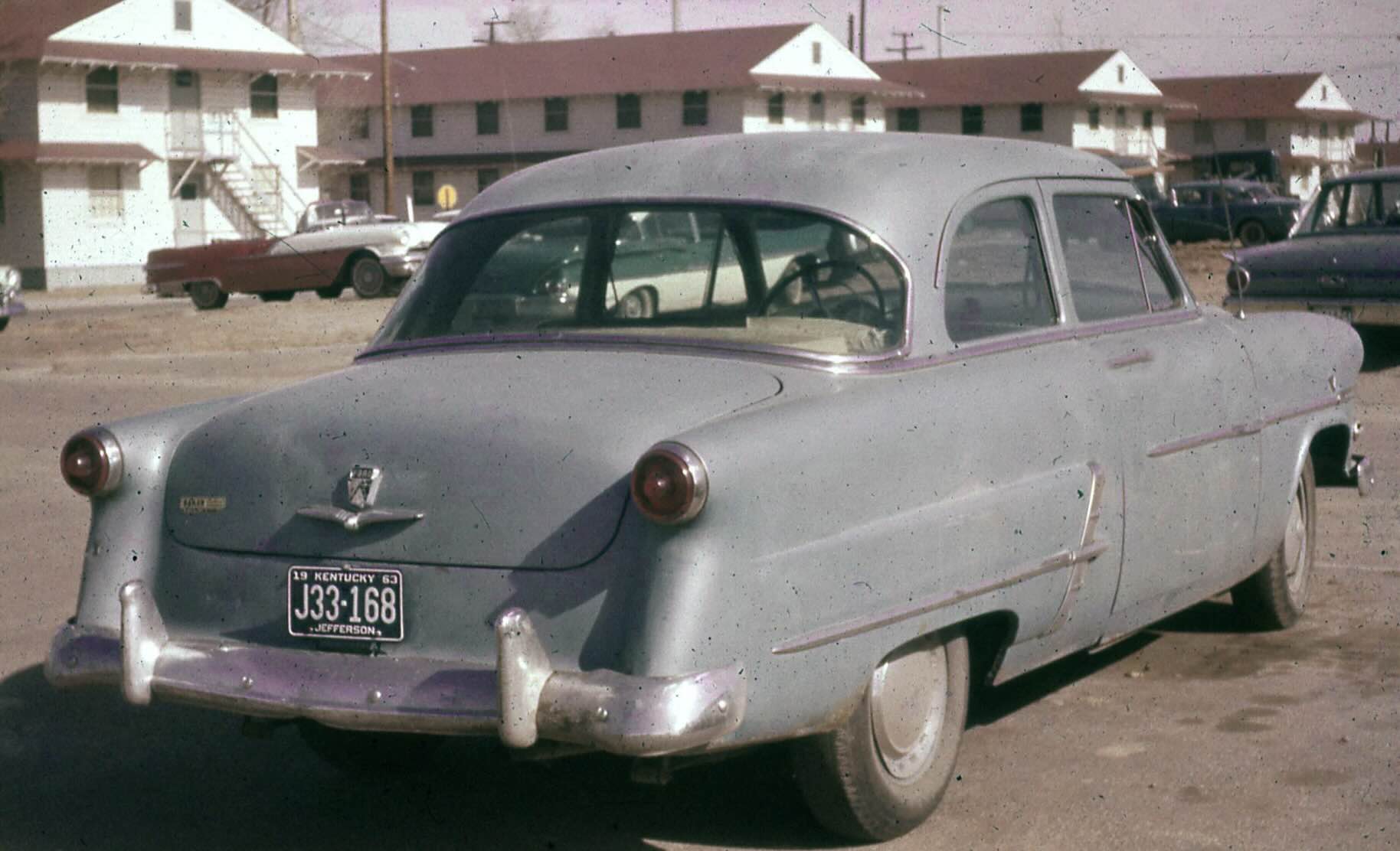 A gray 1950s sedan parked in a lot, featuring a 1963 Kentucky license plate.