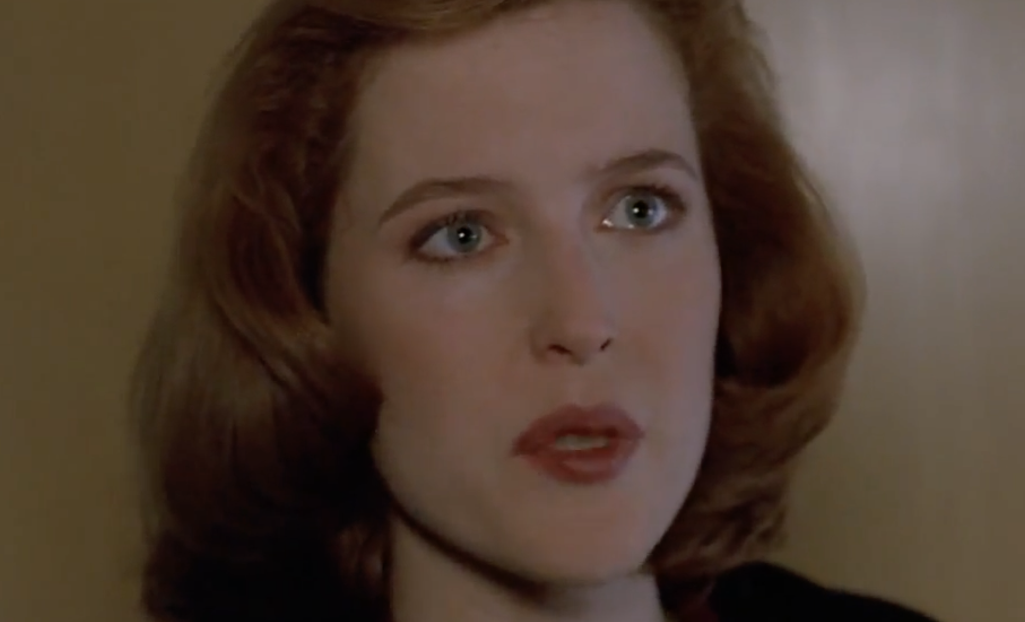 A close-up of a woman with red hair looking forward with a serious expression.