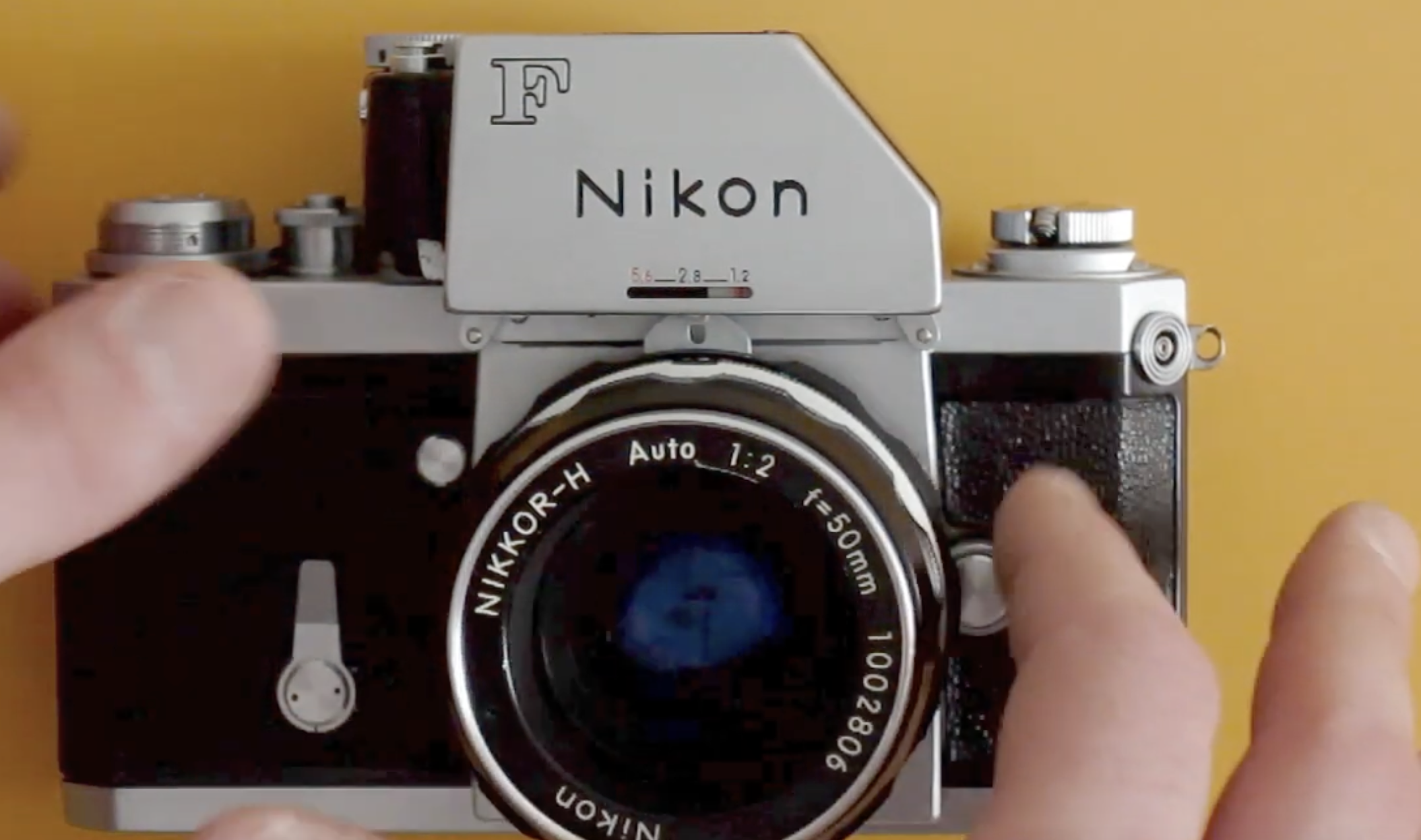 Hands adjusting the settings on a vintage silver Nikon F film camera.