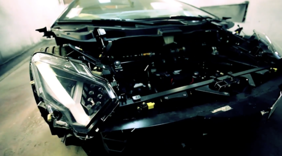 Front view of a sports car with the hood removed, exposing the internal engine bay components and headlights.