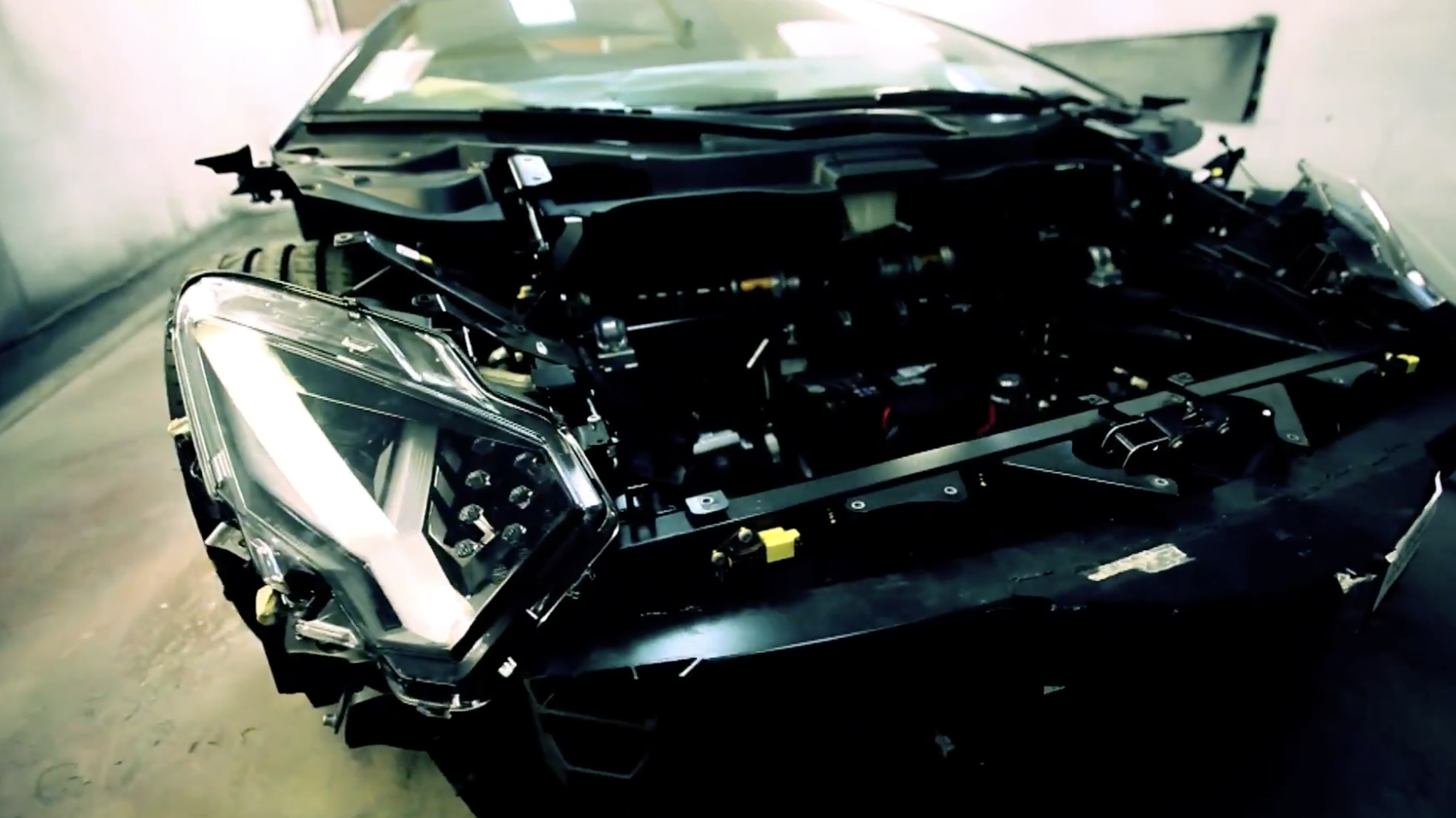 The front end of a luxury sports car with the hood and bumper removed, exposing its headlamp assembly and internal engine components.