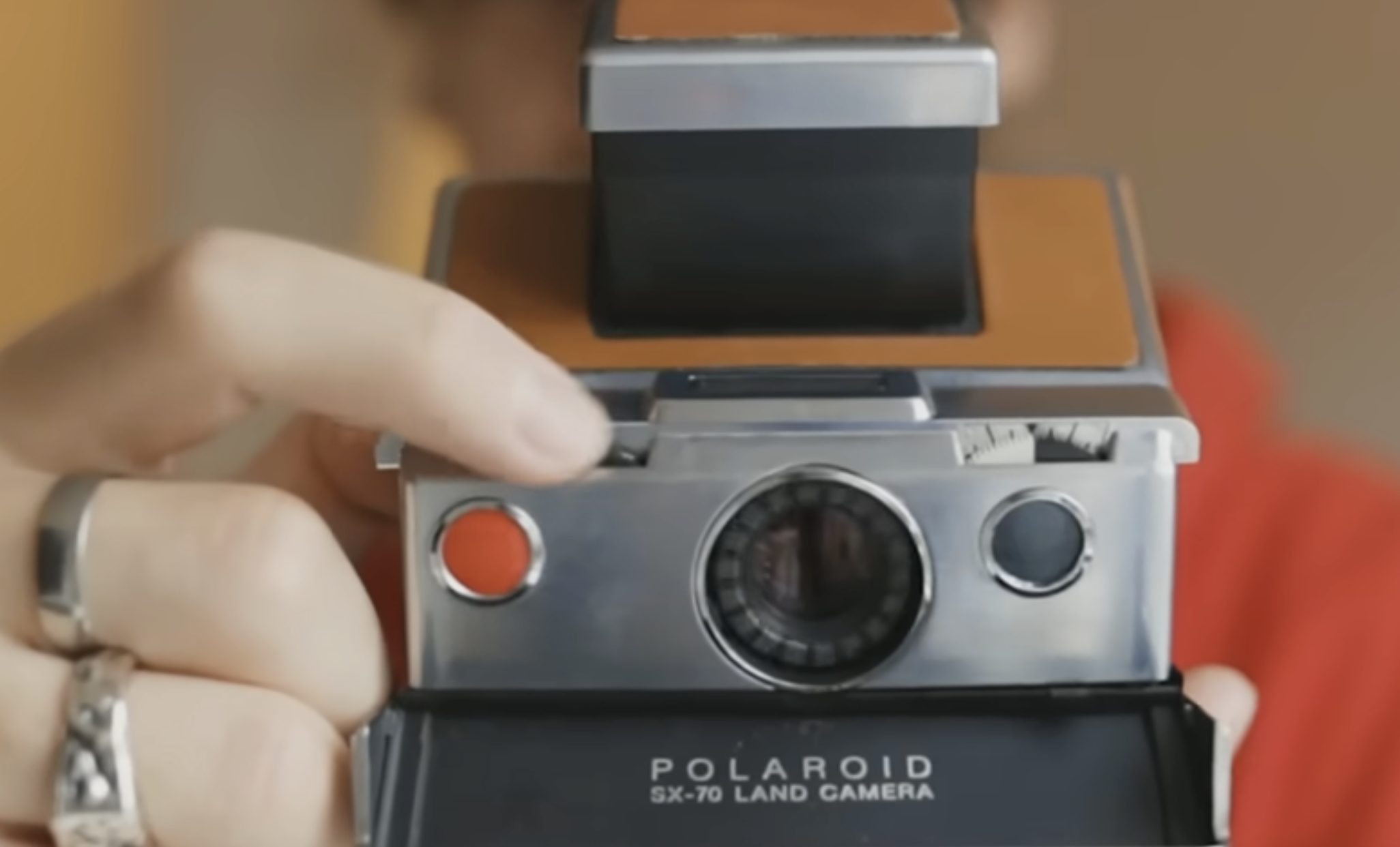 A person holds a silver and tan Polaroid SX-70 Land Camera.