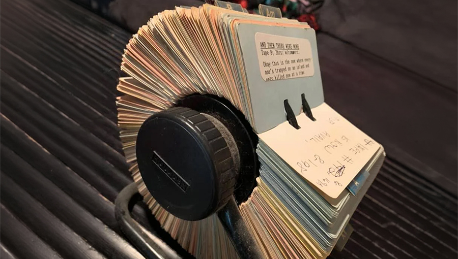 A Rolodex sits on a black desk, filled with index cards organized by tabs, used for storing contact information.