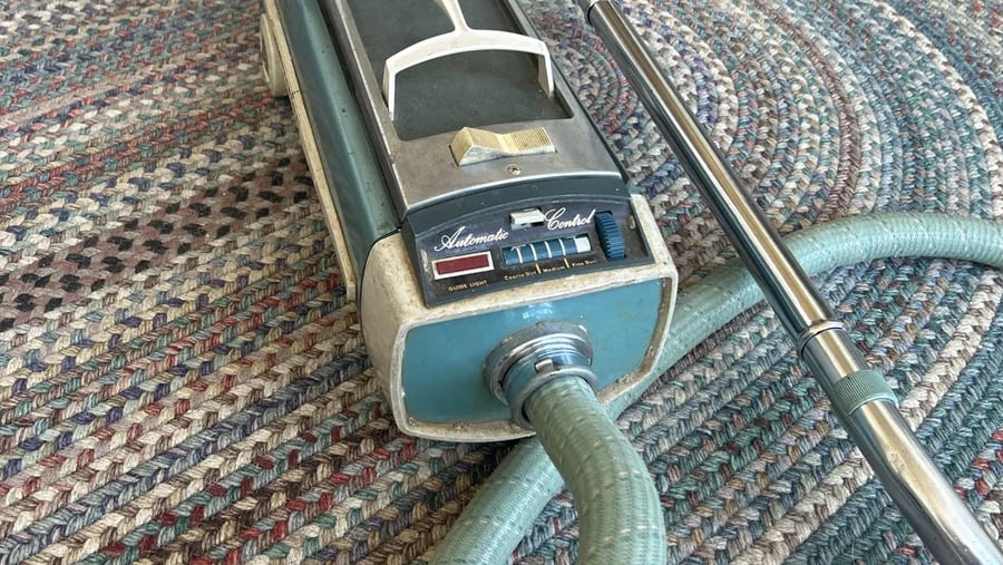 Vintage canister vacuum cleaner with an automatic control panel and attached hose resting on a braided rug.