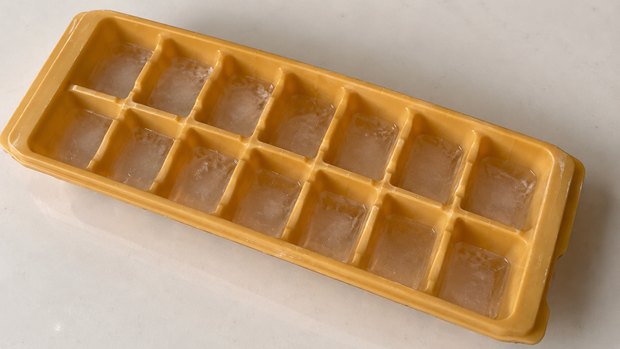 A yellow plastic ice cube tray with fourteen compartments, each filled with ice, rests on a white surface.