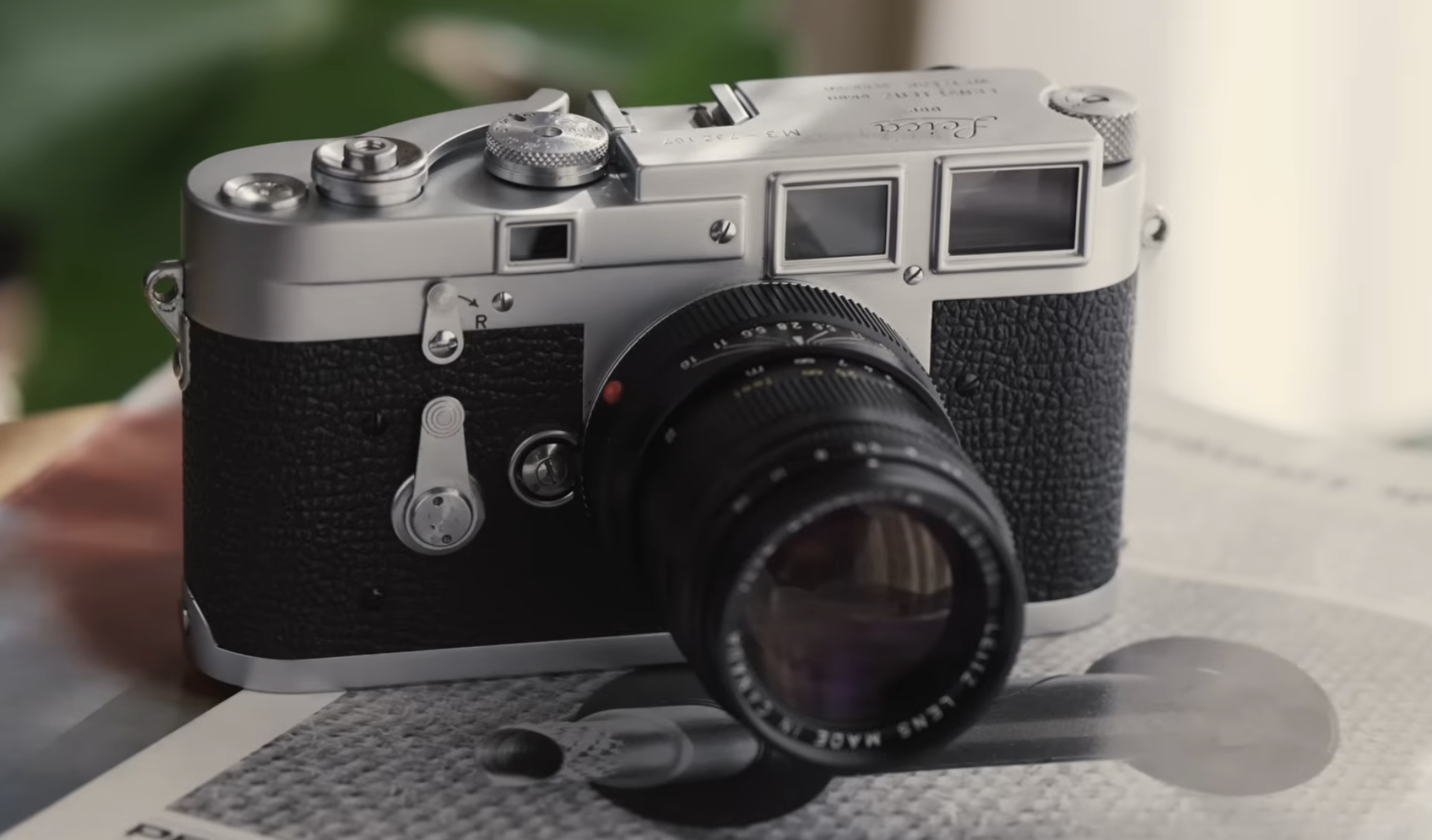 A Leica M3 rangefinder camera with a black lens resting on a printed page.