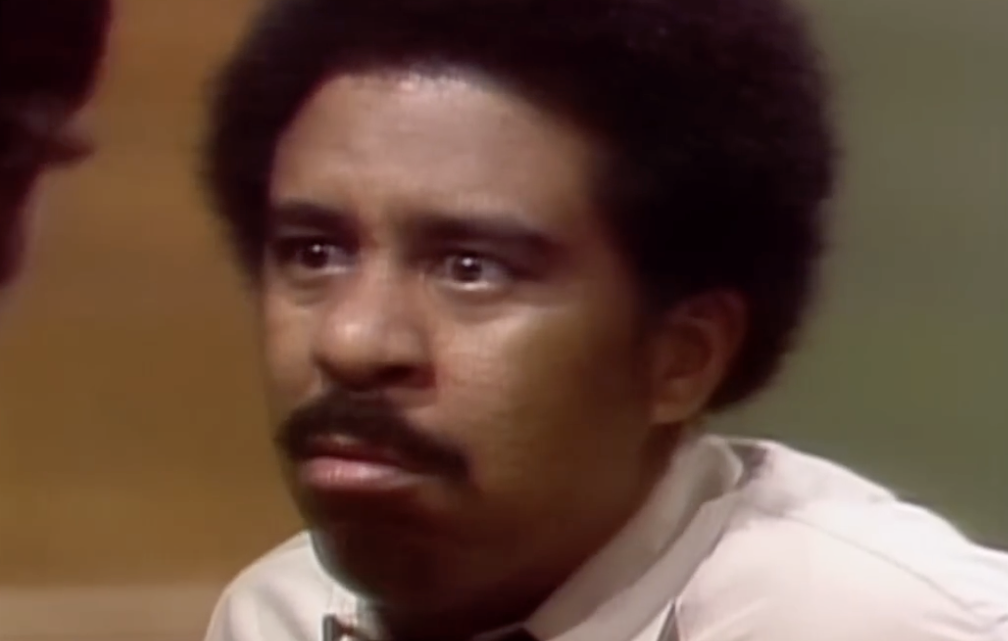A man with a mustache and afro looking intensely at someone off-screen.