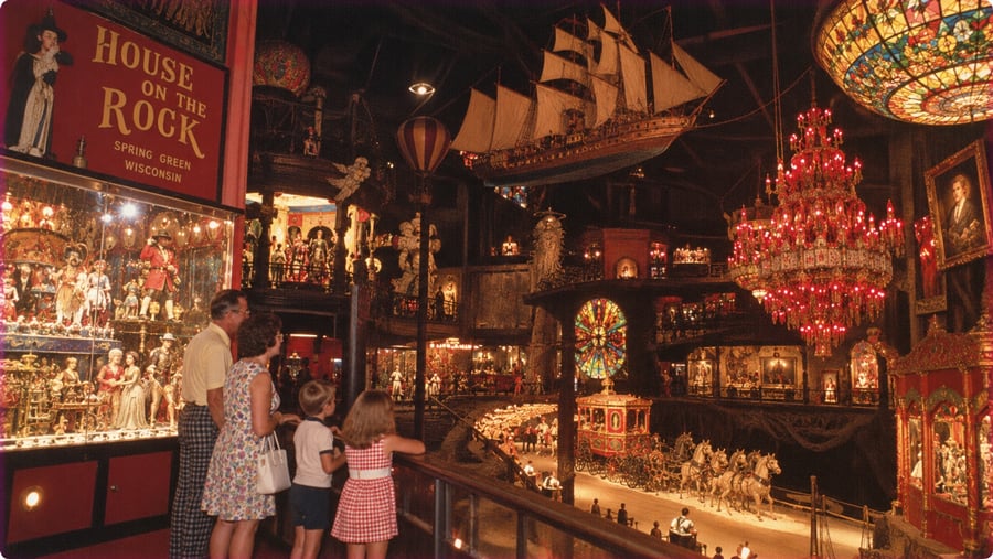 A family views the large, eclectic collection at The House on the Rock, featuring a suspended ship, a red crystal chandelier, and intricate dioramas.