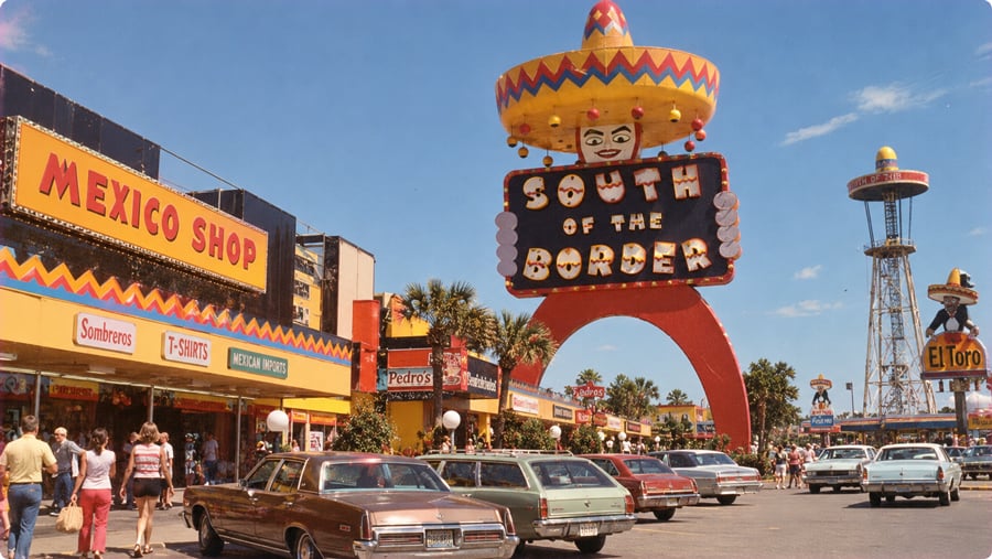 The South of the Border roadside attraction featuring a giant sombrero-topped sign and an observation tower in a parking lot filled with vintage cars.