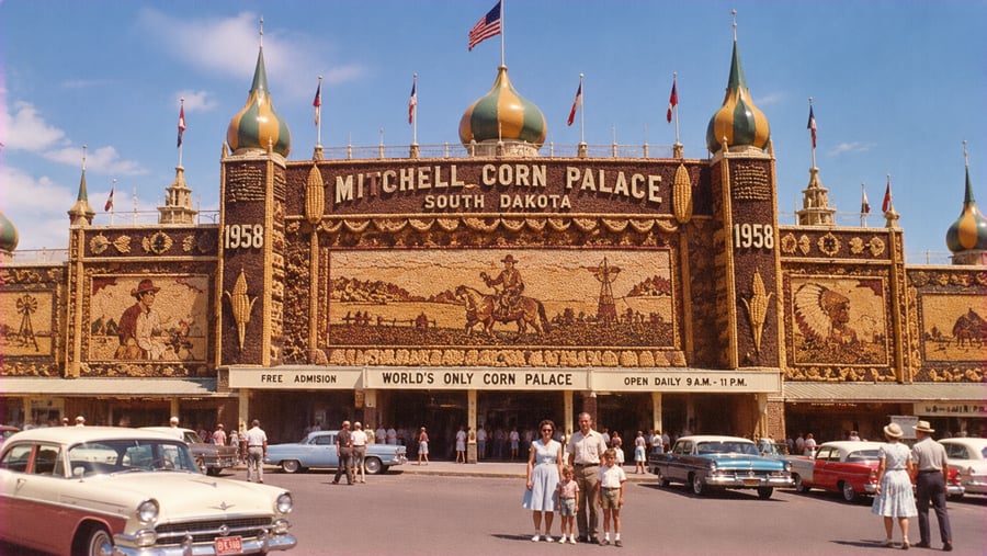The 1958 Mitchell Corn Palace in South Dakota, featuring elaborate corn-husk murals and vintage cars parked in front with visitors standing on the street.