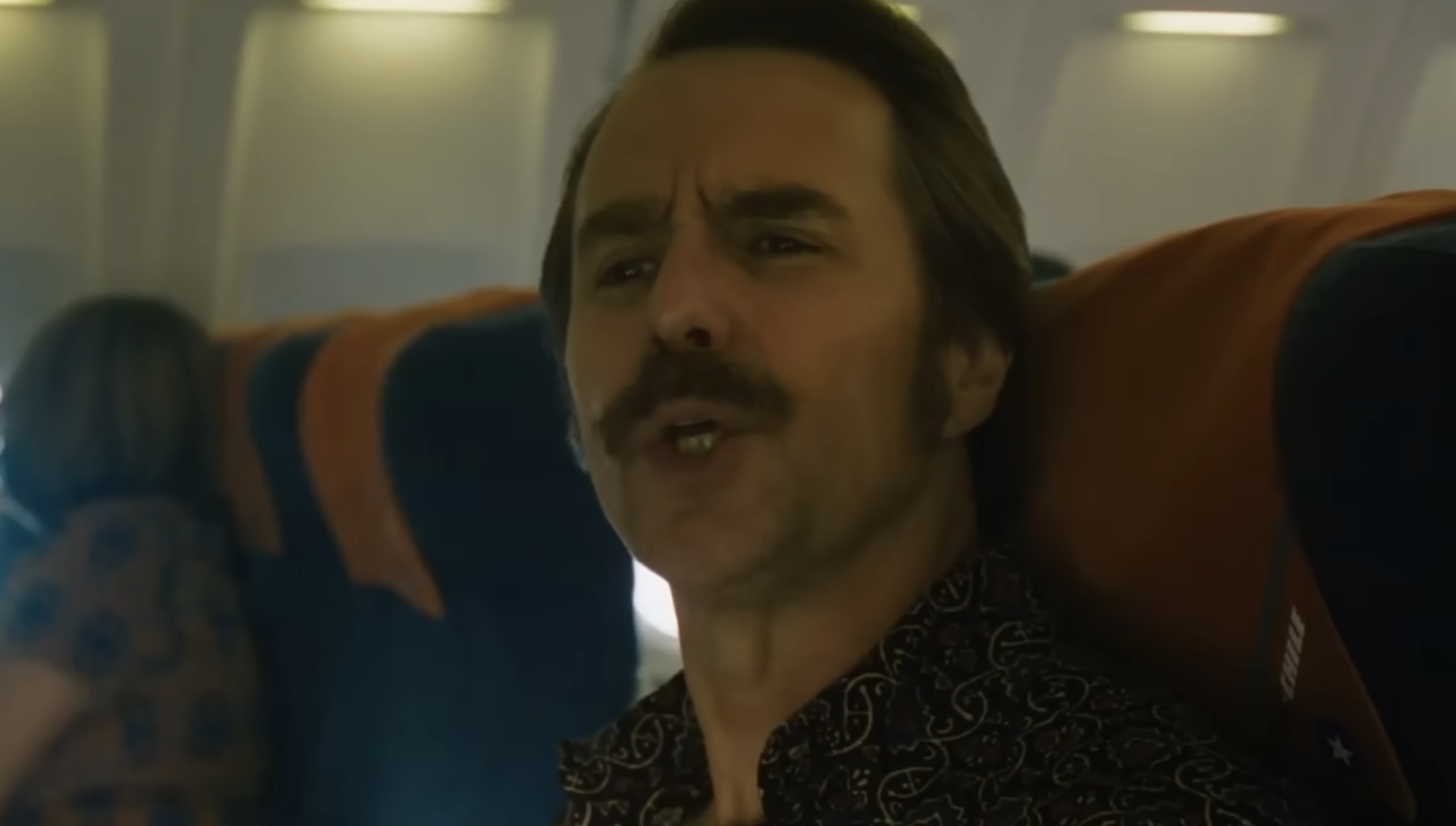 A man with a mustache sitting in an airplane seat.