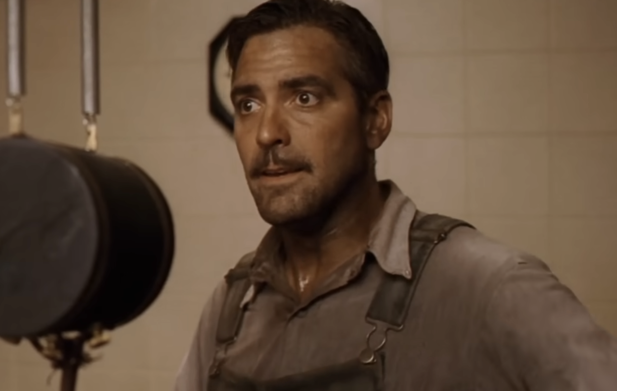 George Clooney as a man in work clothes looks toward the side with a surprised expression.