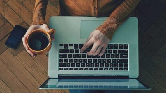 A person using a laptop while holding a mug of coffee.