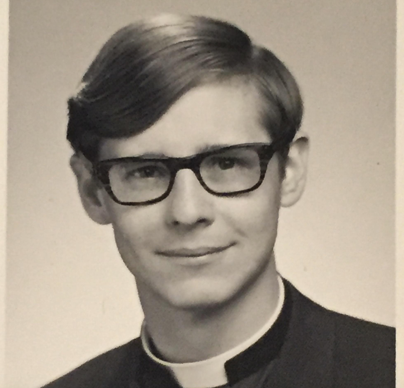 Black and white headshot of a young man wearing glasses and a clerical collar.