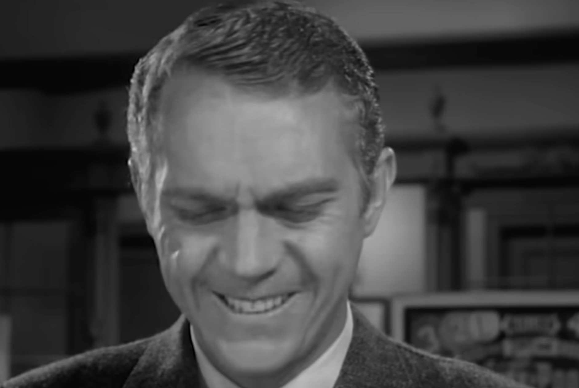 A man in a suit jacket with a grimacing expression.