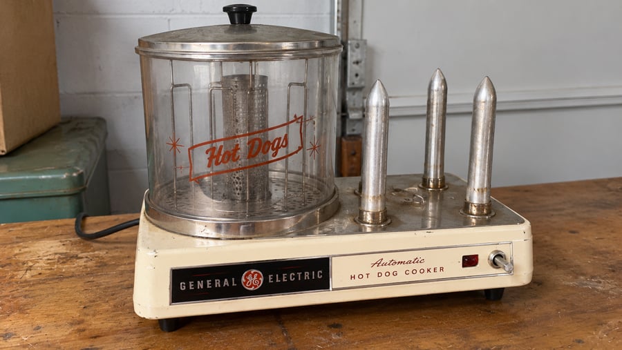 Vintage General Electric automatic hot dog cooker featuring a glass heating chamber and three metal bun spikes.