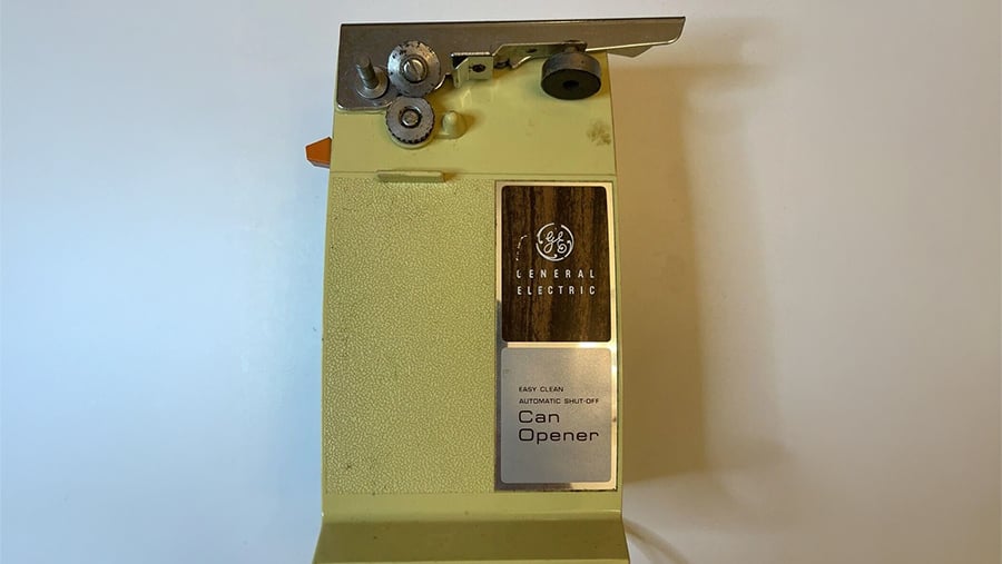 Vintage General Electric electric can opener in light yellow with a metallic cutting mechanism at the top.