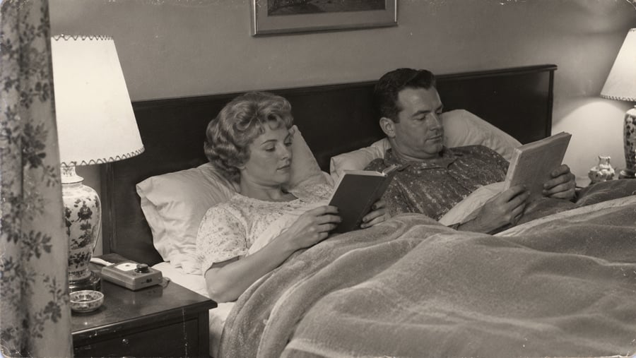 A man and woman sitting in bed at night, each reading a book.