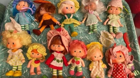 Eleven Strawberry Shortcake dolls in various outfits arranged on a patterned green tray.