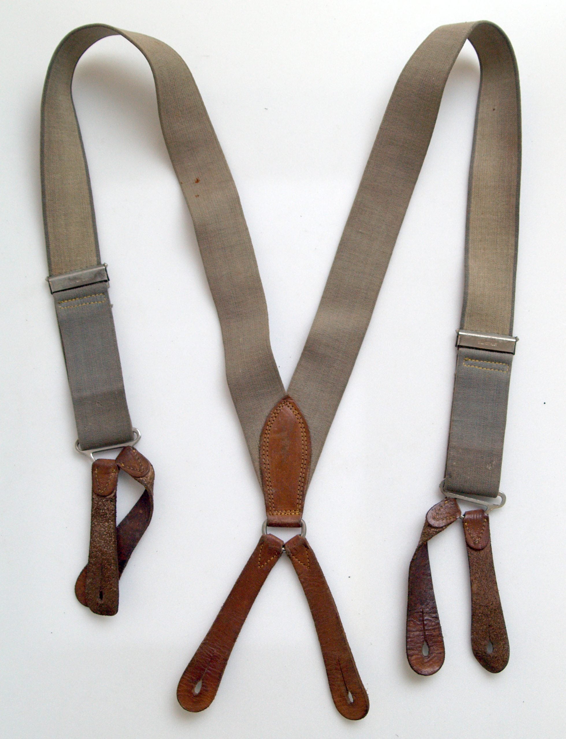 A pair of vintage gray suspenders with leather button loops and metal adjusters, laid flat on a white surface.